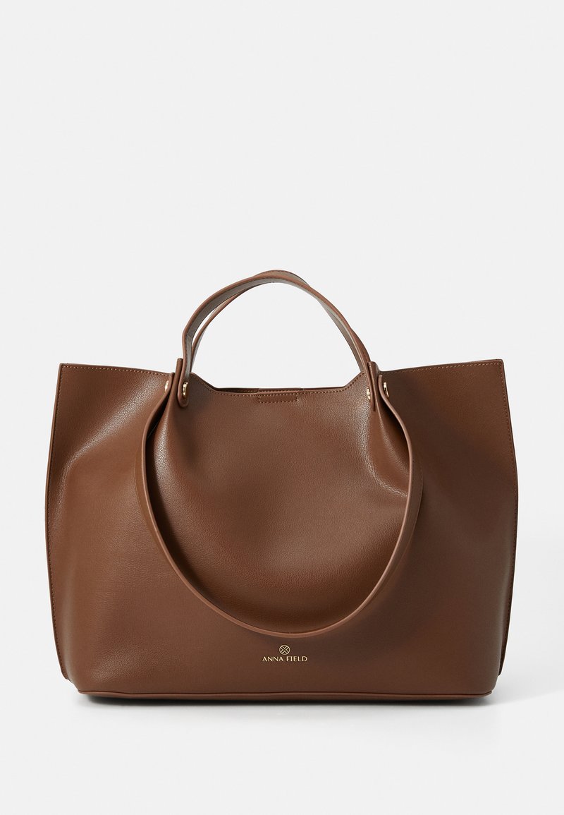 Borsa a spalla in pelle marrone con una texture liscia, grandi manici circolari, caratterizzata da un design minimalista e logo impresso nella parte inferiore.