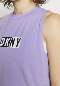 Top senza maniche viola realizzato in tessuto morbido, con il logo bianco e nero "DKNY" sul fronte. Vestibilità leggermente rilassata, texture liscia.