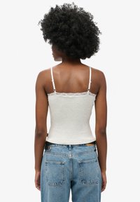 Top de tirantes de canalé gris claro con detalles de encaje; cuenta con tirantes finos y una silueta ajustada. Combinado con jeans de mezclilla azul de talle alto.