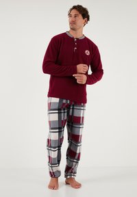 Bordeauxfarbenes Langarmshirt mit grauem Kragen und Knopfleiste, kombiniert mit karierten Hosen in roten, grauen und weißen Tönen; weicher Stoff, lässige Passform.