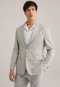 Hellgraue Leinenjacke mit subtilen Karomuster, Ein-Knopf-Verschluss, mit Revers und zwei Taschen. Getragen über einem hellen Hemd.