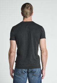 Czarna krótki rękaw t-shirt wykonany z bawełny, z okrągłym dekoltem. Noszony z niebieskimi dżinsami, prezentując swobodny krój.