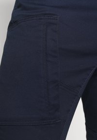 Navyblaue Denim-Cargo-Hosen mit einer Seitentasche, subtiler gerippter Textur und kontrastierenden Nähten entlang der Säume.