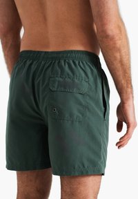 Shorts de bain verts en tissu léger. Dotés d'une taille élastique, de poches latérales et d'une poche arrière avec œillet.
