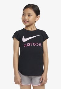 Černé bavlněné tričko s krátkým rukávem, které má velký bílý symbol Nike a růžový text "JUST DO IT." Nosené s šedými šortkami a růžovými akcenty.