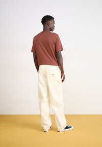 Une chemise courte à manches brunes assortie à un pantalon ample crème. La tenue présente un design simple avec une coupe décontractée et sans motifs visibles.