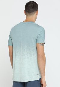 Lyseblå atletisk t-shirt med en gradient fra mørkere til lysere ved kanten. Har korte ærmer og en glat stoftekstur.