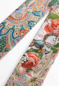Tissu à motifs arborant des designs floraux et ornementaux vibrants, incluant un cheval, dans des couleurs vives comme le rose, le vert et l'orange.