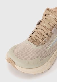 Beige trening sko med mesh-overdel og gummisåle. Har teksturerte detaljer og et fremtredende snøresystem. Rund tå for komfort.