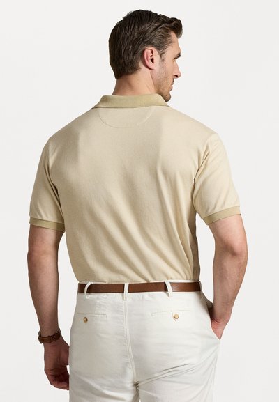 Beige polo shirt met een gestructureerd patroon, korte mouwen en een contrasterende kraag. Gecombineerd met witte broek en een leren riem in bruin.