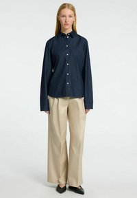 Tamsiai mėlyna džinsinė marškinėliai su ilgomis rankovėmis, derinami su grietinėlės spalvos plačiomis kelnėmis ir juodais lygiais bateliais. Paprastas dizainas be matomų raštų.