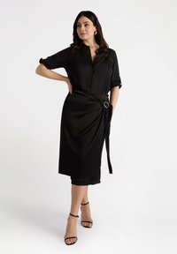 Zwart overhemdjurk met opgerolde mouwen, afgesloten met een brede ceintuur met een grote ronde gesp, structuurstof, rok tot de knie.