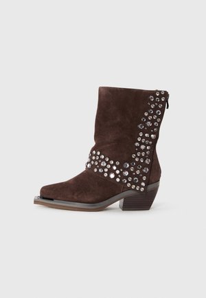 Botte en suede marron mi-mollet avec un petit talon empilé, décorée de strass argentés et noirs regroupés sur le côté et à l'avant.