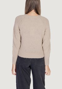 Maglione lavorato a maglia beige con un motivo a pallini testurizzato, scollo rotondo e polsini e orlo a costine. Abbinato a pantaloni scuri e larghi.