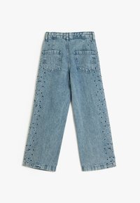 Vaaleansiniset farkut, joissa on leveä lahje, kaksi takataskua ja koristeelliset helmiyksityiskohdat ulkolahkeissa.