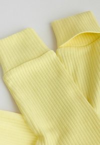 Prim-plan al unei țesături galbene pliabile din tricot nervurat, prezentând linii verticale texturate și manșete moi și elastice.