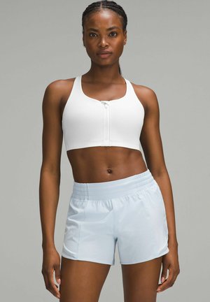 Sujetador deportivo blanco con cierre frontal, de textura suave, combinado con pantalones cortos atléticos de cintura elástica en azul claro, con un ajuste holgado y relajado.