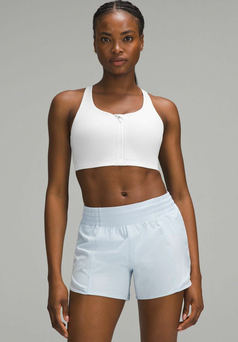 Sujetador deportivo blanco con cierre frontal, de textura suave, combinado con pantalones cortos atléticos de cintura elástica en azul claro, con un ajuste holgado y relajado.