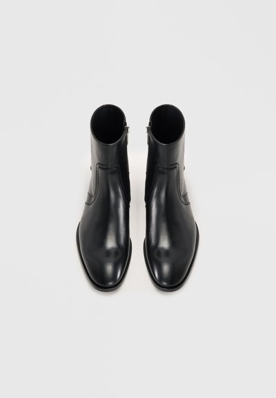 Ett par svarta läderankelboots med sidodragkedjor, spetsiga tår och subtila sömsdetaljer, visade från en uppifrån-blick.
