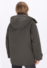 Dunkelgrüne, isolierte Jacke mit Kapuze, die eine glatte Textur, Seitentaschen und Druckknopf-Details aufweist. Rückansicht gezeigt.