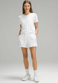 Camiseta de algodón blanca combinada con pantalones cortos blancos de cintura elástica, con bolsillos laterales y un diseño relajado. Usada con zapatillas deportivas blancas.