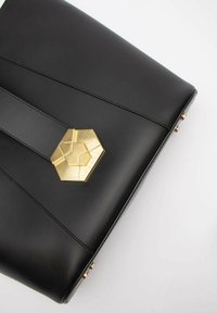 Czarna skórzana torebka z sześciokątnym złotym akcentem i usztywnioną konstrukcją; gładka tekstura z detalami haftu.