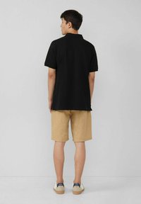 Schwarzes Poloshirt mit kurzen Ärmeln, kombiniert mit beigen Shorts. Das Outfit wird mit weißen Sneakers mit marineblauen Akzenten abgerundet.