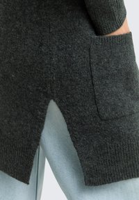 Pulover din lână gri închis cu manșete ribbed și o buzunare frontală, având un detaliu cu tiv împărțit; asortat cu blugi din denim albastru deschis.