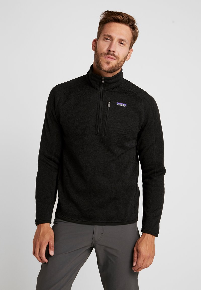Schwarzer Fleece-Pullover mit einem Viertelreißverschluss und hohem Kragen, ausgestattet mit einem kleinen lila Patagonia-Logo auf der Brust. Glatte Textur.