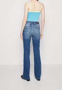 Blå ribbad tanktopp med spetsdetaljer, i kombination med medelblå, utsvängda denimjeans med hög midja och bakfickor.