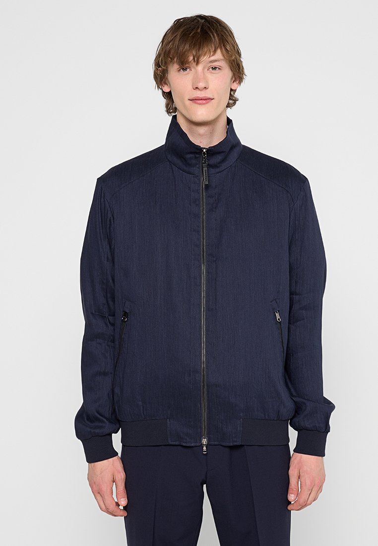 Marineblaue Bomberjacke mit hohem Kragen, Reißverschluss, zwei Seitentaschen, gerippten Bündchen und einem strukturierten Stoff.