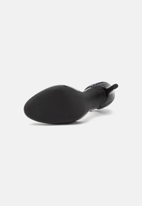 Stivaletto in pelle nera visto dal suola con un leggero tacco e linguetta sul retro su sfondo bianco.