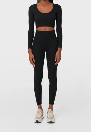 Black long-sleeve crop top paired with high-waisted leggings. Fitted design, textured fabric. Footwear features a light color with black accents.