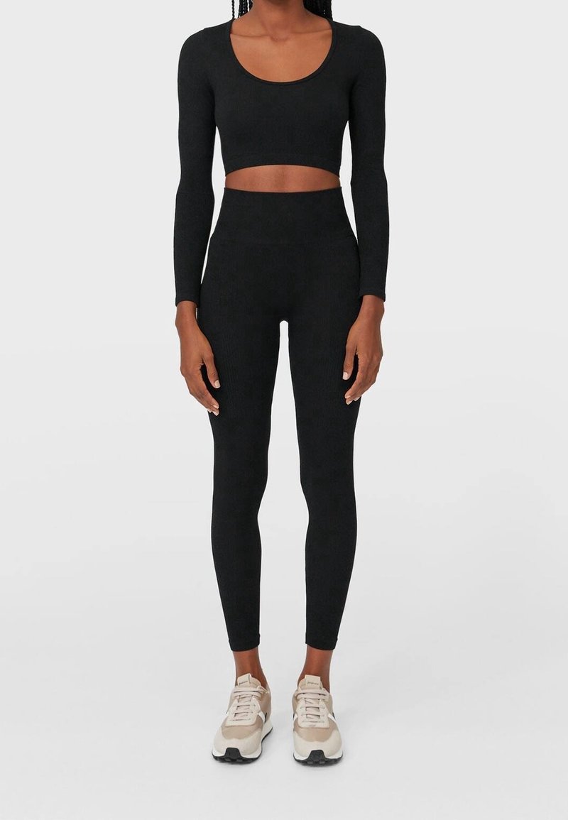 Black long-sleeve crop top paired with high-waisted leggings. Fitted design, textured fabric. Footwear features a light color with black accents.