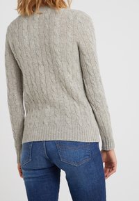 Vaaleanharmaa palmikkoneulepusero, jossa on resorit hihoissa ja helmassa, esitetään takaa, yhdistettynä sinisiin farkkuihin. Kuvioitua kangasta, istuva malli.