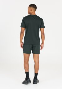 Mörkgrön träningströja och shorts med en strukturerad väv, korta ärmar och en avslappnad passform, tillsammans med svarta träningsskor och strumpor.