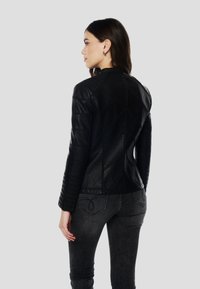 Giacca in pelle nera con design aderente, caratterizzata da spalle trapuntate e una cucitura curva sulla schiena. Abbinata a jeans scuri e aderenti.