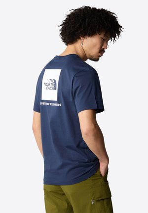Marineblå bomulds T-shirt med korte ærmer. Har et hvidt firkantet logo på ryggen, teksten "EVERYTOP EXPLORING," og en rund halsudskæring.