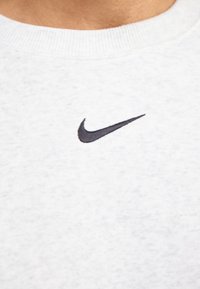 Sudadera gris claro con una textura suave, presenta un pequeño logo negro de Nike en el pecho y un cuello redondo clásico.