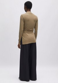 Langsleeve top in lichtbruin, met een getailleerd ontwerp en geplooide zijdetails. Gepaard met loose-fitting zwarte wijde broek.