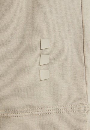 Material bej cu textură canelată, având trei mici taburi pătrate aliniate vertical. Coaserea este vizibilă pe margine.