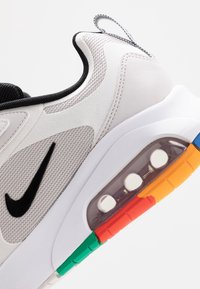 Nike-sneakers med ett vitt och grått mesh-övre, svarta detaljer och en genomskinlig luftenhet med flerfärgade detaljer på sulan.