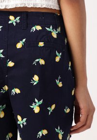 Pantalones azul marino con un patrón de limones, que presentan limones amarillos con hojas verdes y flores blancas. Incluyen un detalle de bolsillo trasero.