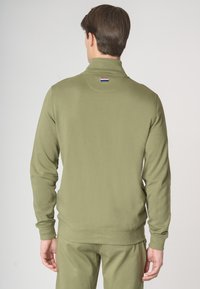 Felpa verde oliva con colletto alto, polsini e orlo a costine, e una piccola etichetta con logo sul retro. Realizzata in un tessuto liscio e morbido.
