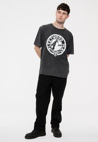 Gray oversized t-shirt with a circular white graphic print featuring a hand holding a microphone, paired with black pants and black shoes.