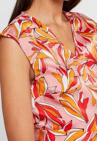 Blomstret ærmeløs top i pink med orange og røde bladmønstre. Glat stof med V-halsudskæring og subtile skulderdetaljer.