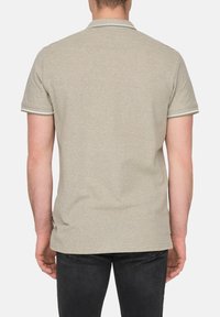Lichtbeige polo-shirt van een gestructureerde stof, met een contrasterende lichtgroene streep op de kraag en mouwen. Zwarte jeans zijn gedeeltelijk zichtbaar.