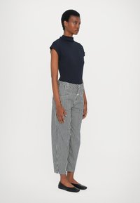 Top de cuello alto tipo mock navy, con mangas cortas, combinado con pantalones de pierna ancha a rayas blancas y negras. Zapatos planos negros. Diseño sencillo, silueta ajustada.