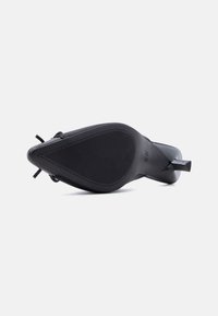 Μαύρο ψηλοτάκουνο παπούτσι, φαίνεται από τη σόλα, με υφή αντιολισθητικού καουτσούκ και μυτερό μπροστινό μέρος με λεπτό τακούνι στιλέτο σε απλό φόντο.