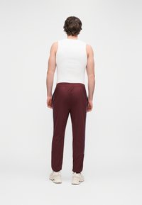 Bordó színű nadrág kék oldalsávokkal, rugalmas derékrésszel és mandzsettás szárvégekkel, fehér ujjatlan felsővel és világos sportcipővel párosítva.